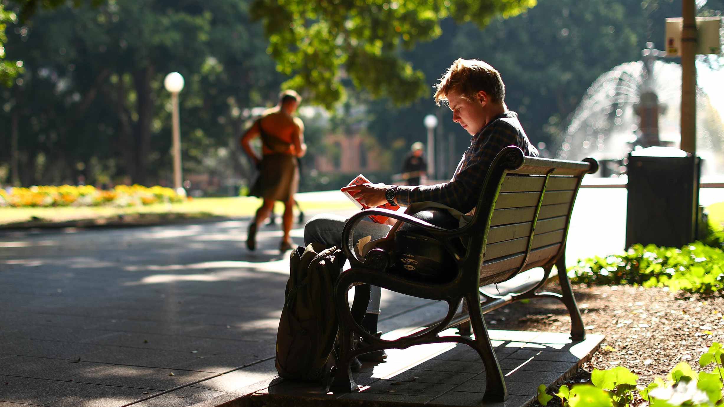 Person sitting on a park bench reading a book and enjoying the morning sun